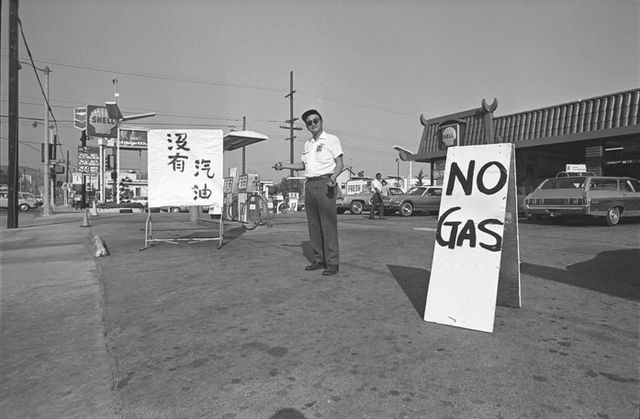 A gas station attendant stands between signs reading 'No Gas' in English and Chinese during the 1973 oil crisis
