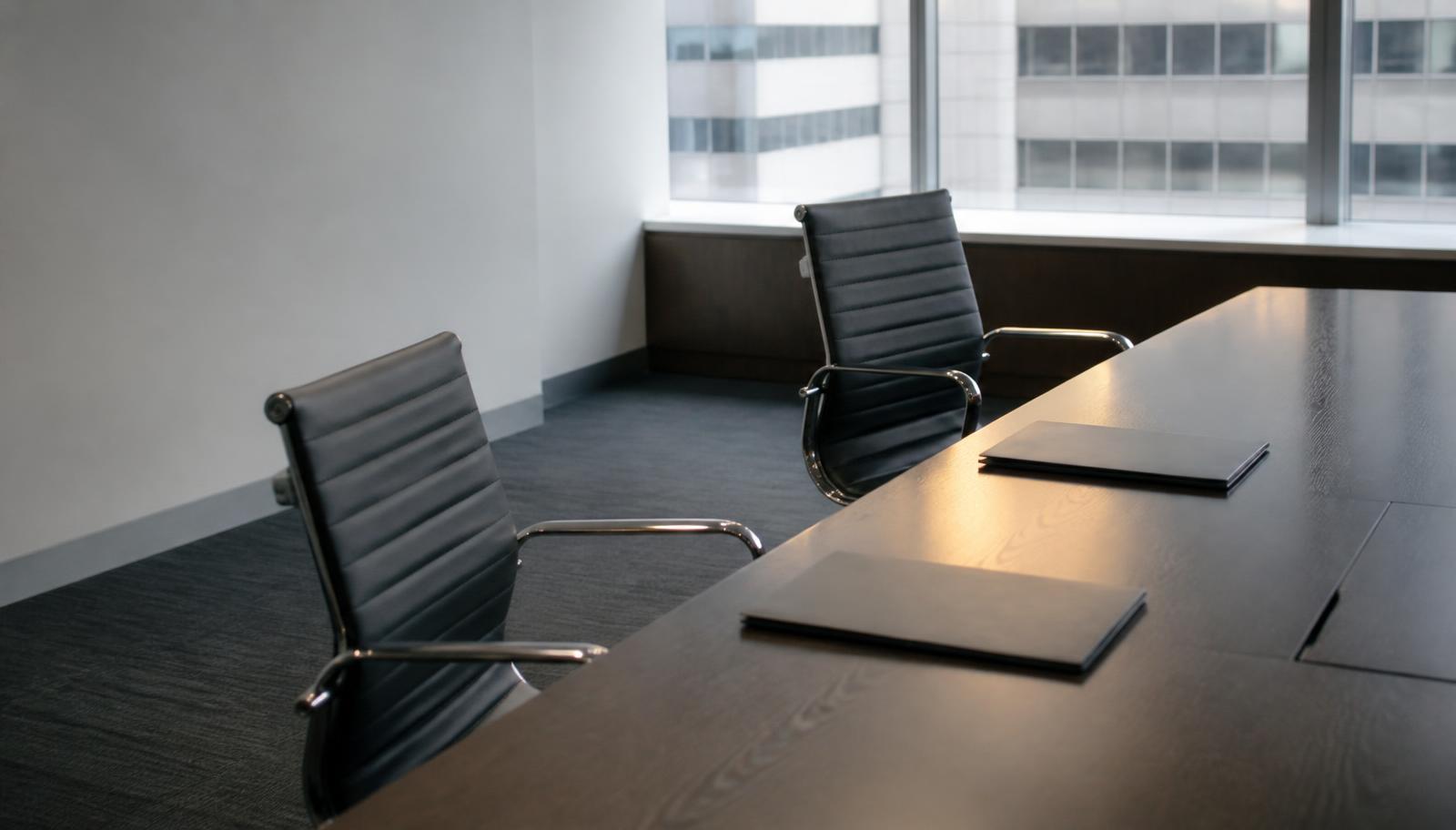 A boardroom table with one chair pushed back and empty, illustrating a business partner breaching a contract